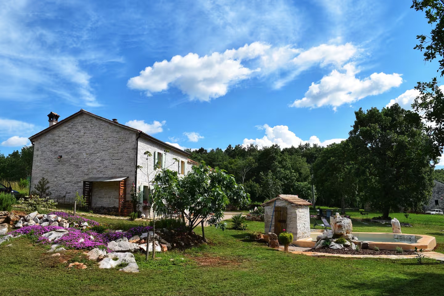 La casa in pietra e la piscina circondate da prato, fiori e alberi secolari